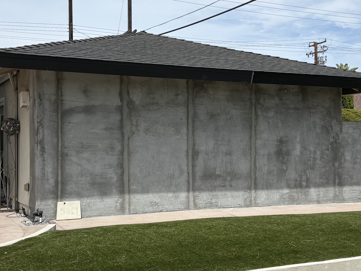 After: exterior wall re-stuccoed with a new concrete curb and turf edge