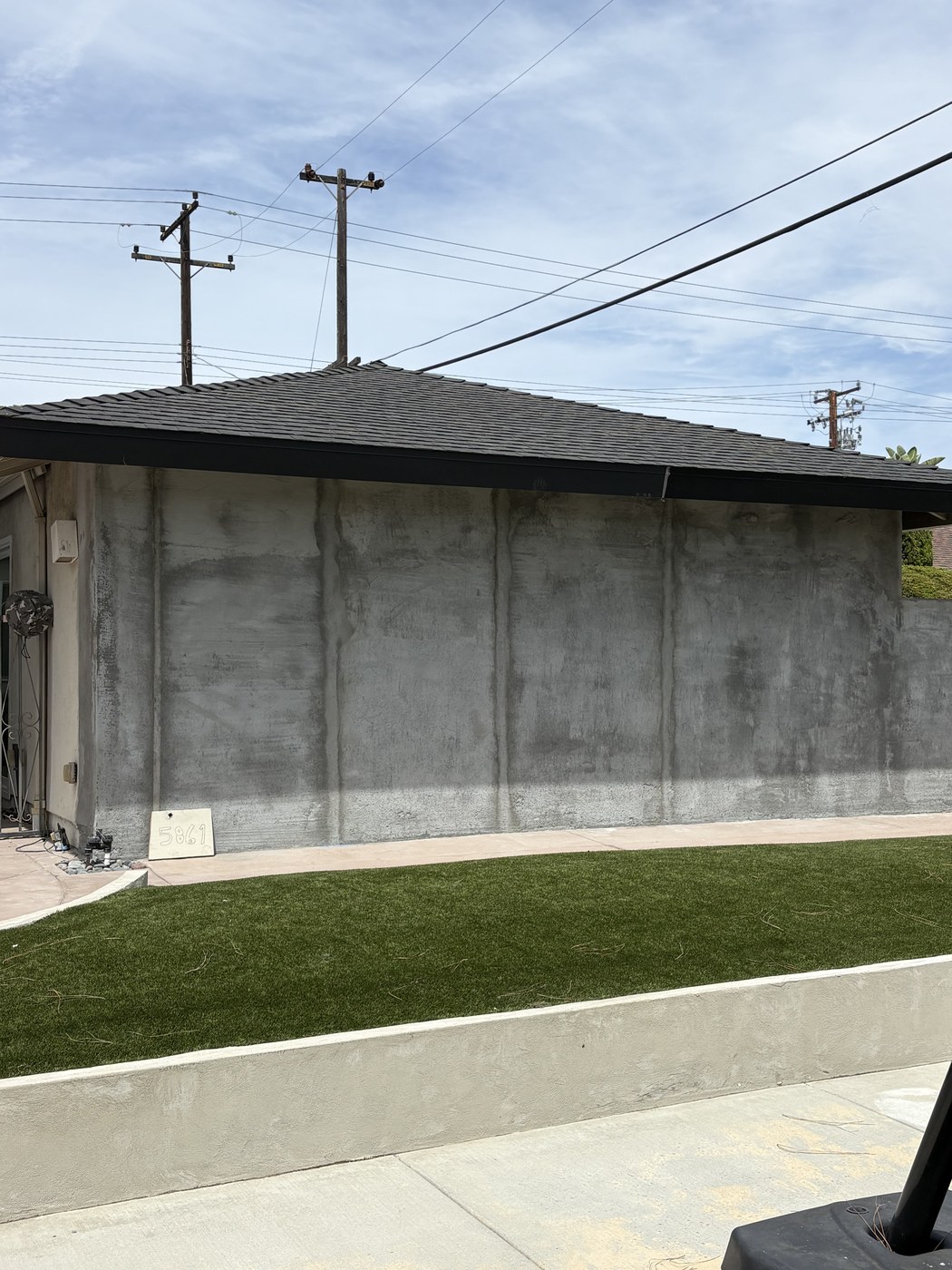 Side wall freshly re-stuccoed next to a new concrete curb and turf edge