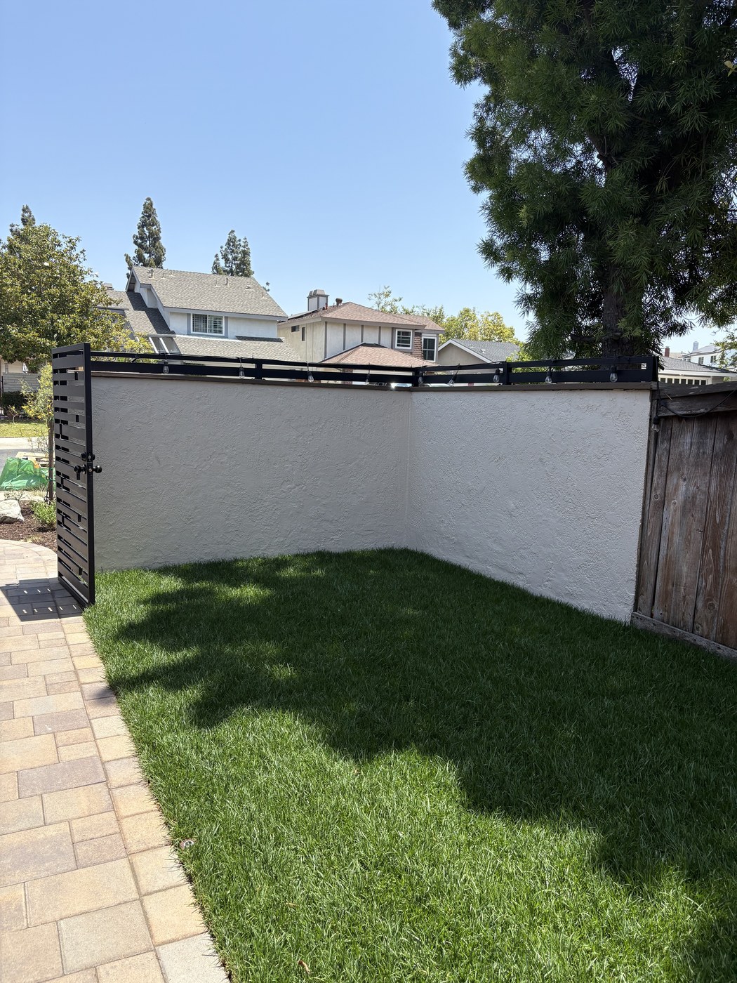 Backyard corner with a freshly painted stucco wall, new turf and a new fence